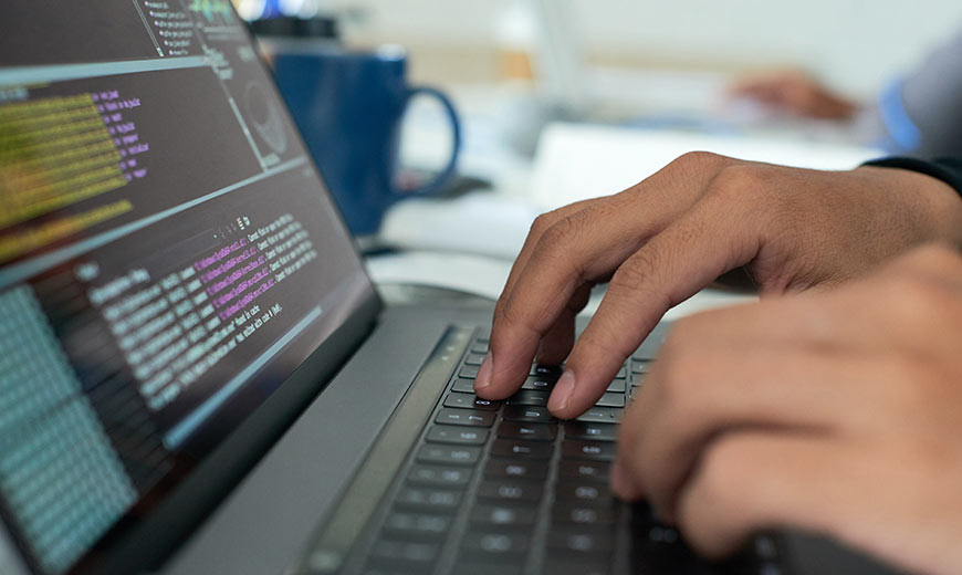 Hands on laptop displaying code lines.