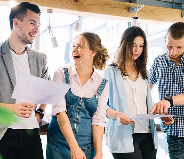 Four people smiling and looking at papers in colleague's hands.