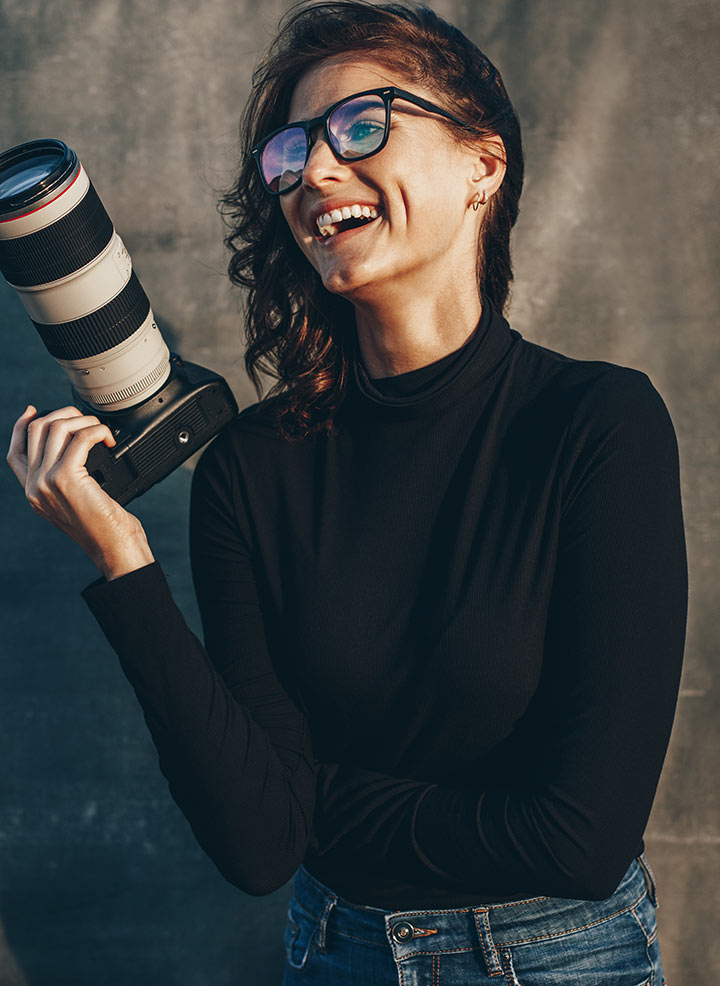 Woman with glasses and camera in her hand smiling and posing.