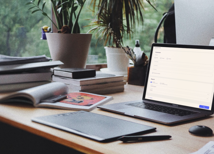 A laptop on a desk, surrounded by books and desk-flowers, displaying a part of an app developed for a client.